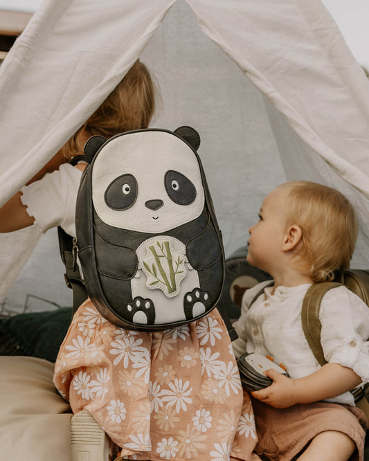 Vaikai žaidžia palapinėje, vienas jų su vaikiška kuprine pandos formos, kitas laikydamas žaislinį fotoaparatą